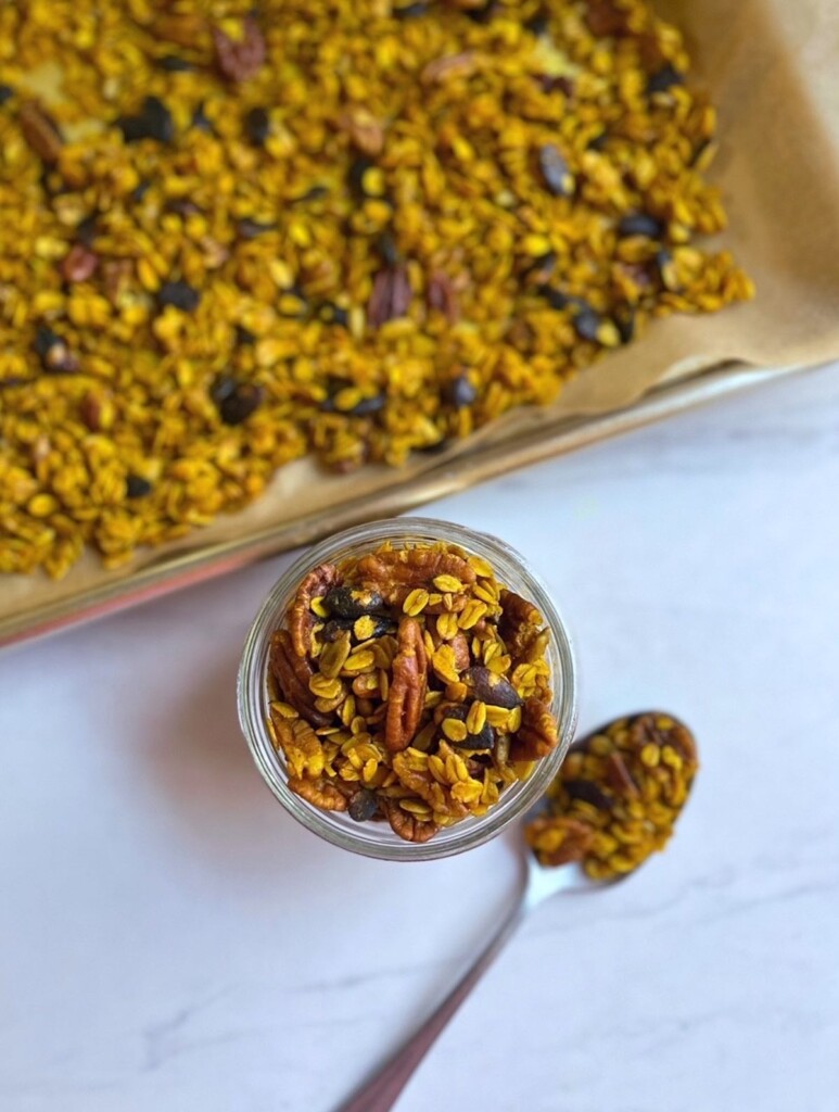Overhead shot of a jar of Golden Spiced Granola next to a sheet pan of granola