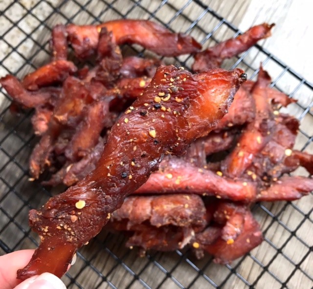 Close-up view of a piece of turkey jerky with a platter of jerky behind it.