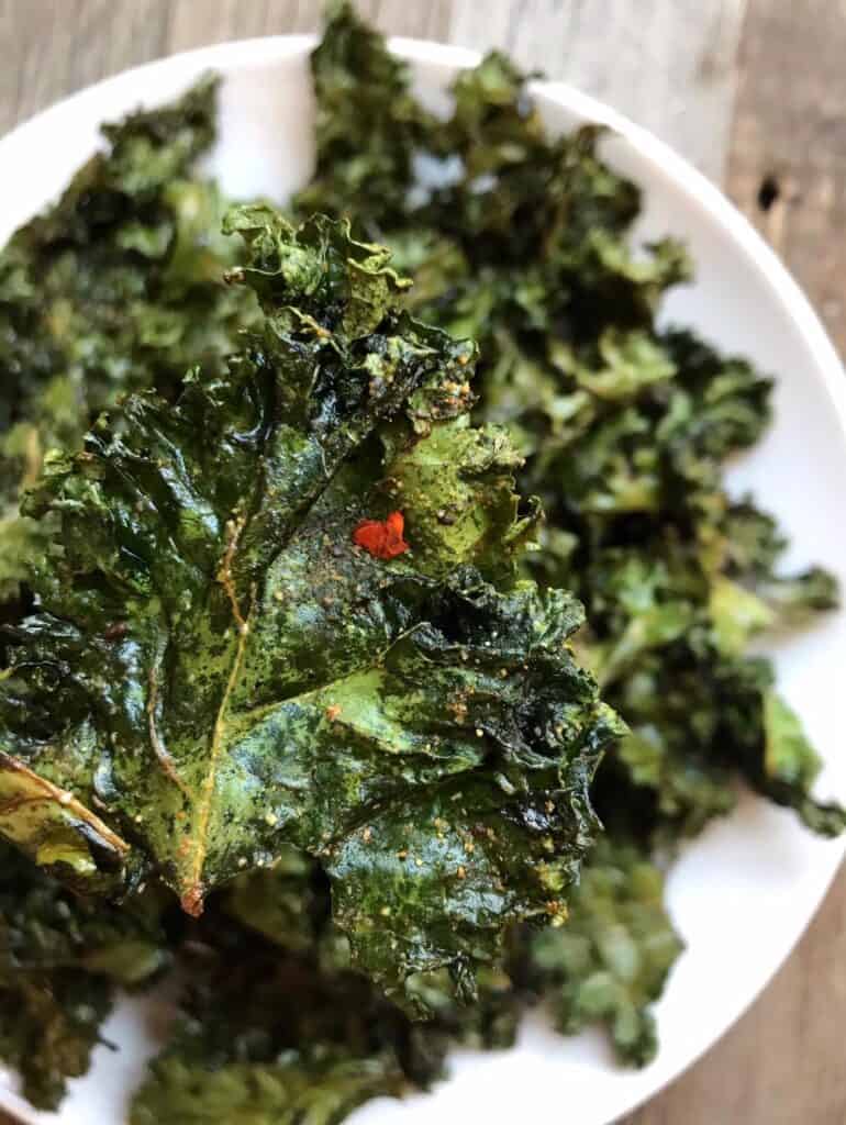 Close-up shot of a Crispy Baked Kale Chip above a plate of chips