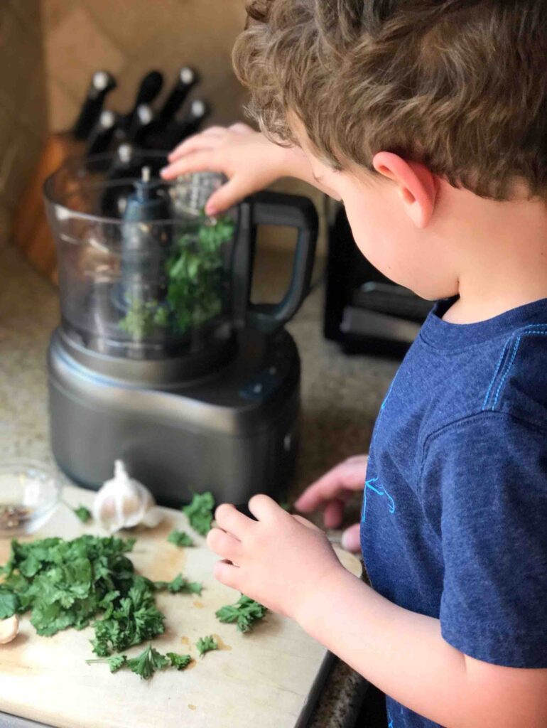 Boy placing chimichurri ingredients into a food processor