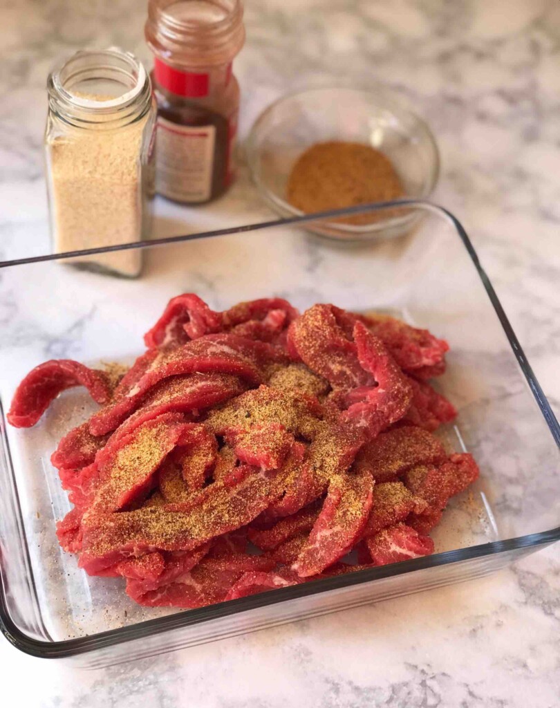 Strips of steak in a glass jar with a dry rub on top