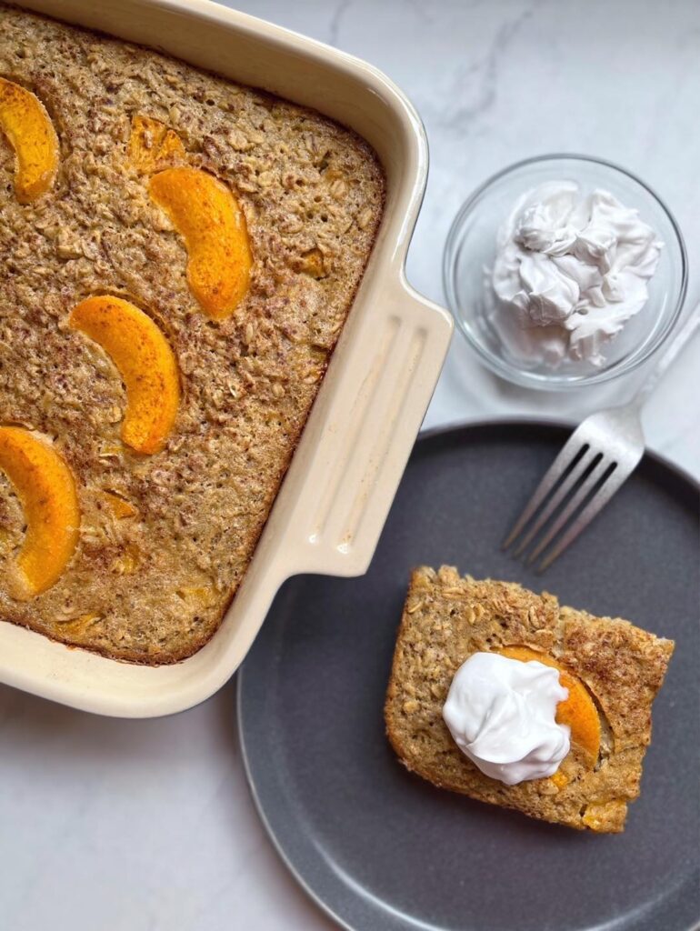 Overhead shot of slice of Peaches and Cream Baked Oatmeal next to pan of oatmeal