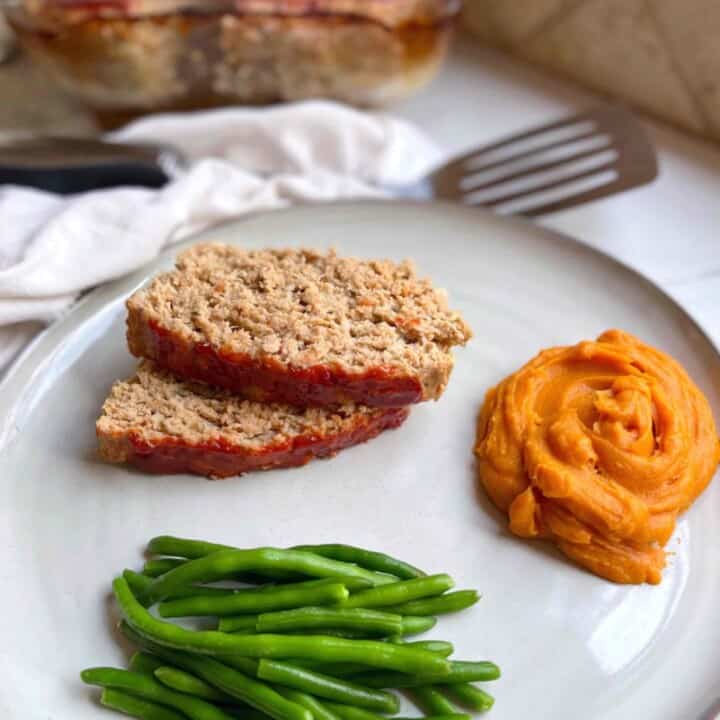 Slices of meatloaf on a plate with green beans and potato mash